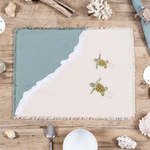 A rectangular beach-themed placemat with a sage green and cream color-blocked design, white lace trim along the border, and two embroidered sea turtles on the cream side, 