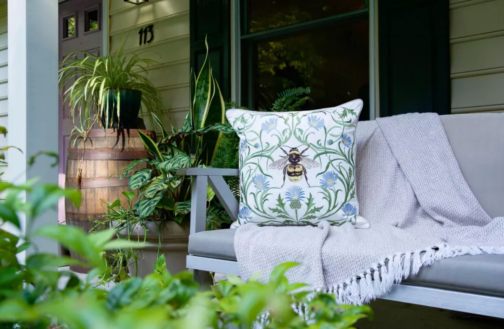 A decorative throw pillow with a bumblebee and blue flowers on a green vine pattern.