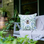 A decorative throw pillow with a bumblebee and blue flowers on a green vine pattern.