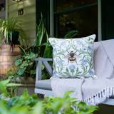 A decorative throw pillow with a bumblebee and blue flowers on a green vine pattern.
