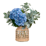 An artificial floral arrangement featuring a large blue hydrangea bloom, green and silver eucalyptus leaves, and a woven natural fiber basket vase.