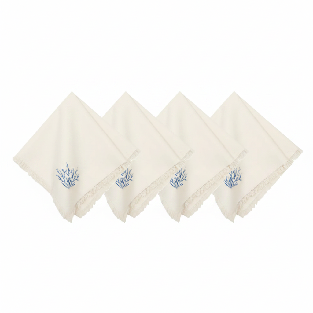 Four off-white cotton napkins with fringed edges and a small blue botanical embroidery on the corner.