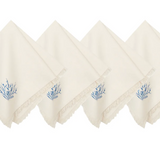 Four off-white cotton napkins with fringed edges and a small blue botanical embroidery on the corner.