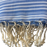 A close-up of a blue and white striped woven textile with fringed tassels along the bottom edge.