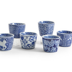 Six blue and white patterned ceramic cups arranged on a white background, with three taller cups behind three shorter cups. The cups feature various floral and decorative blue motifs.