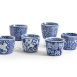 Six blue and white patterned ceramic cups arranged on a white background, with three taller cups behind three shorter cups. The cups feature various floral and decorative blue motifs.