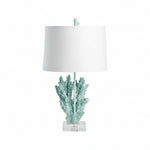 A table lamp with a blue resin and crystal base in the shape of coral, topped with a white lampshade.