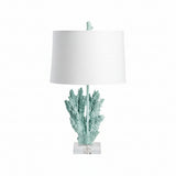 A table lamp with a blue resin and crystal base in the shape of coral, topped with a white lampshade.