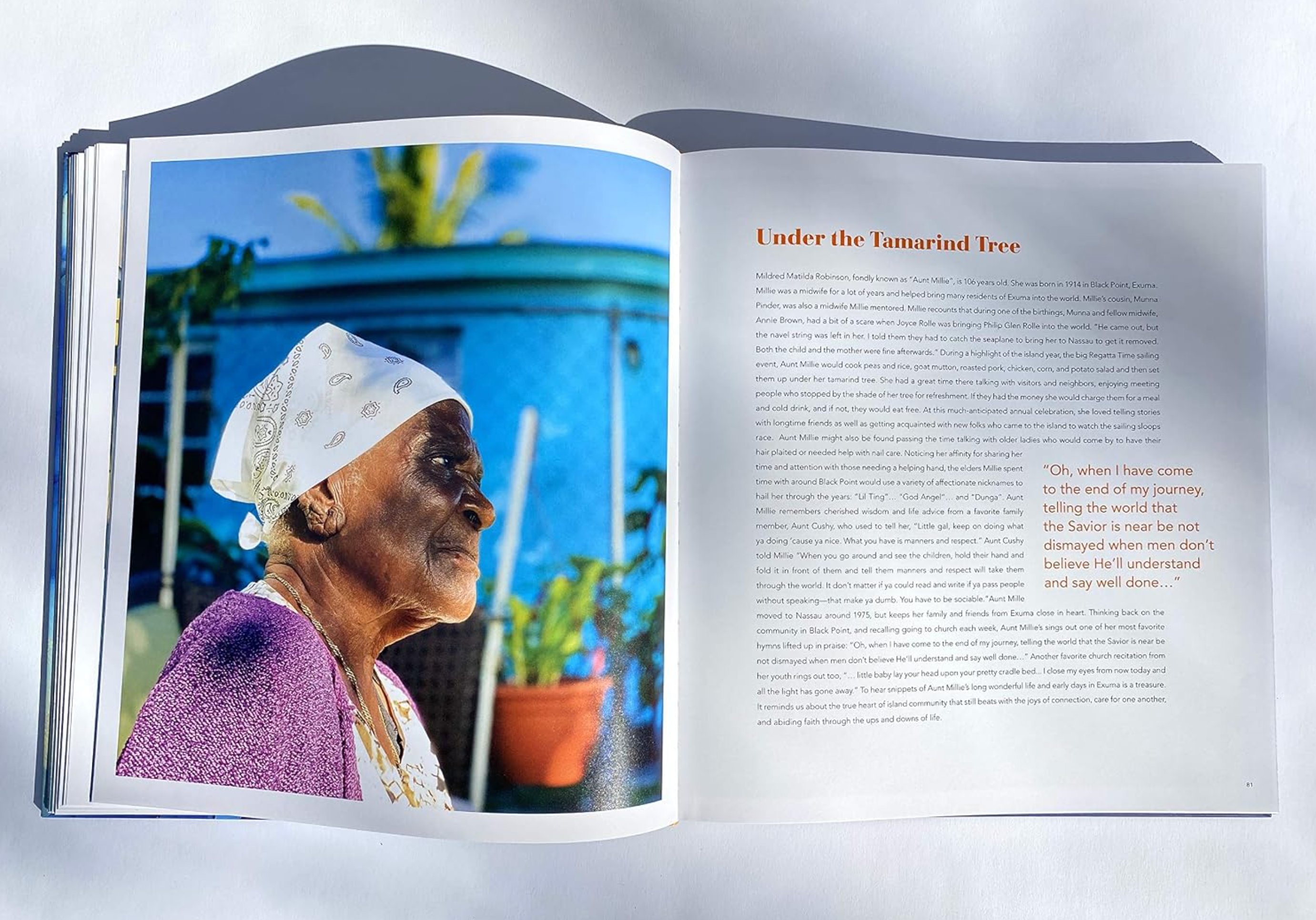 An open printed book or magazine spread photographed against a light gray background. The left page shows a color photograph of an elderly woman in profile wearing a white headscarf and purple garment, with blue sky and plants in the background.