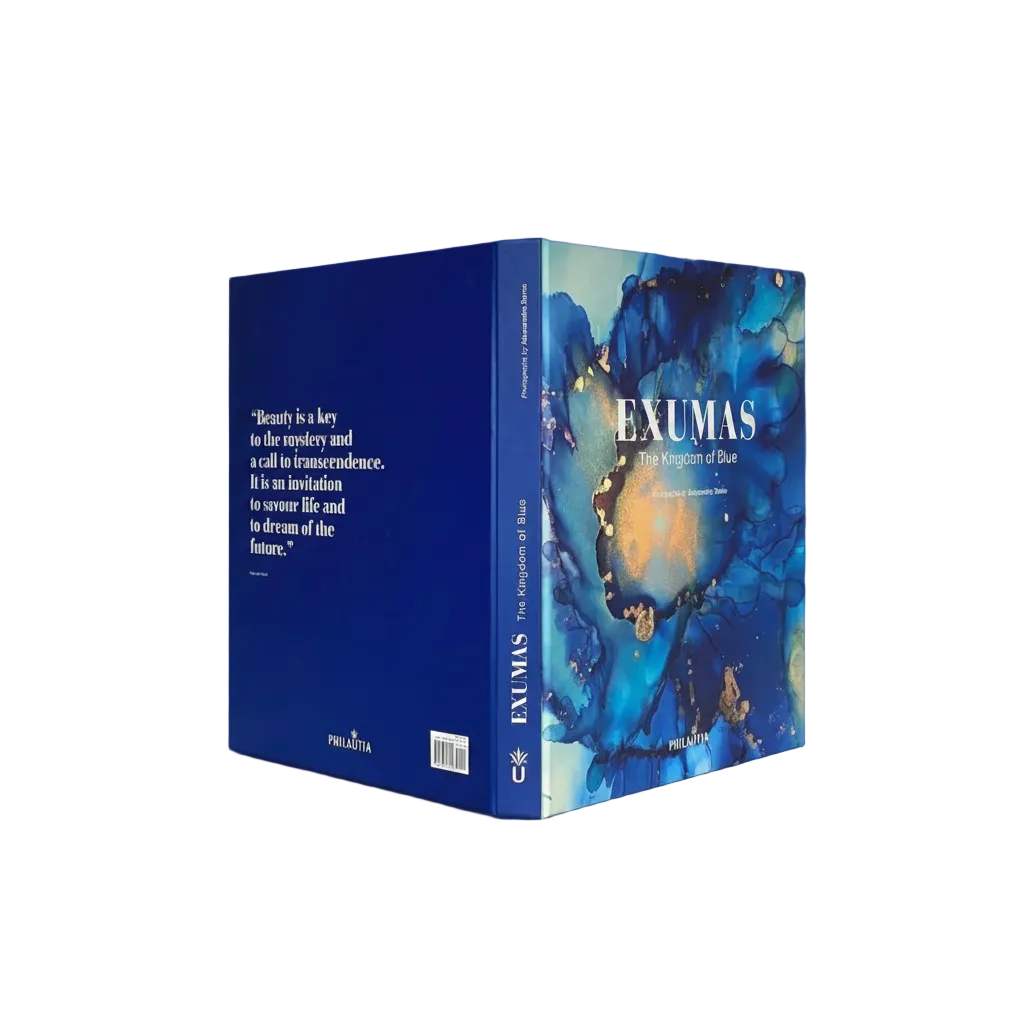 The book 'Exumas: The Kingdom of Blue' by Philastria, shown in a three-quarter view displaying both the front cover and the spine. The cover features an abstract blue and gold marbled design, and the spine is a solid deep blue with white text.