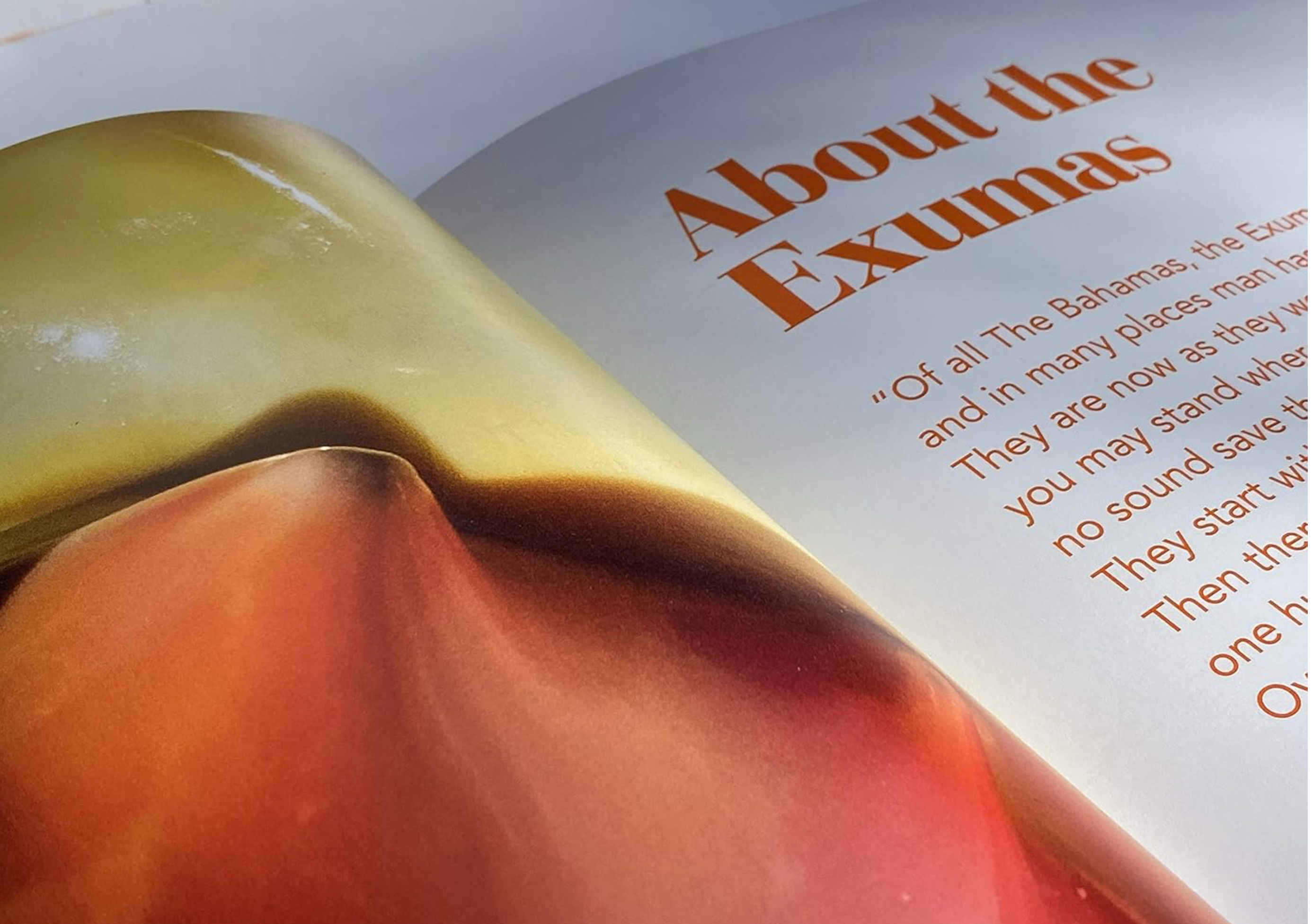 An open book or magazine page showing a close-up photograph of a red and orange flower, with the headline 'About the Exumas' printed in brown text on the right page.