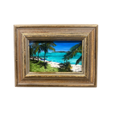 A framed tropical beach landscape painting featuring turquoise water, white sand, palm trees, and a blue sky, housed in a distressed brown wooden frame.