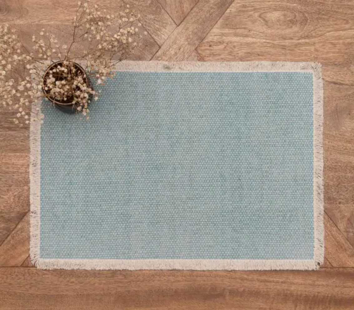 A rectangular light blue woven rug with a natural beige fringed border.