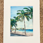 Art print of a tropical scene with palm trees and a beach.