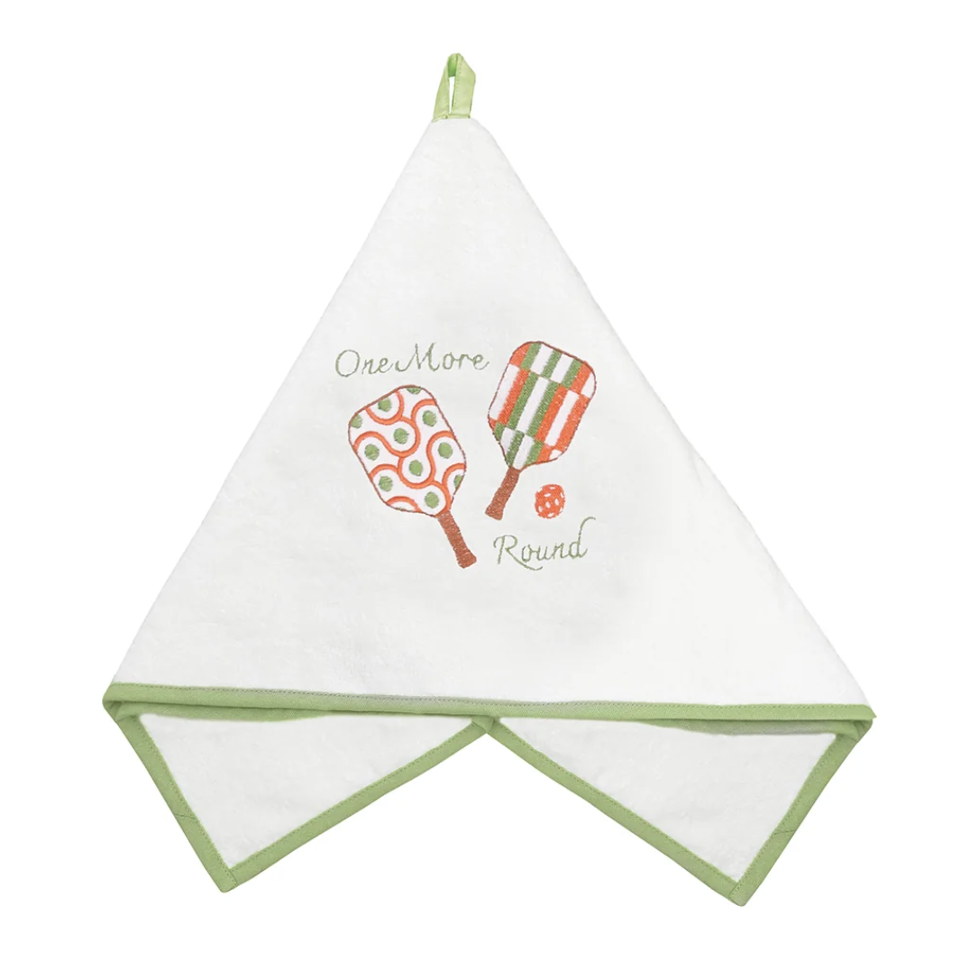 A white cotton kitchen towel with sage green trim, featuring a retro graphic of two tennis rackets and the text 'One More Round' in green and orange.
