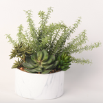 An artificial succulent and shrub arrangement in a round white marble-look planter.