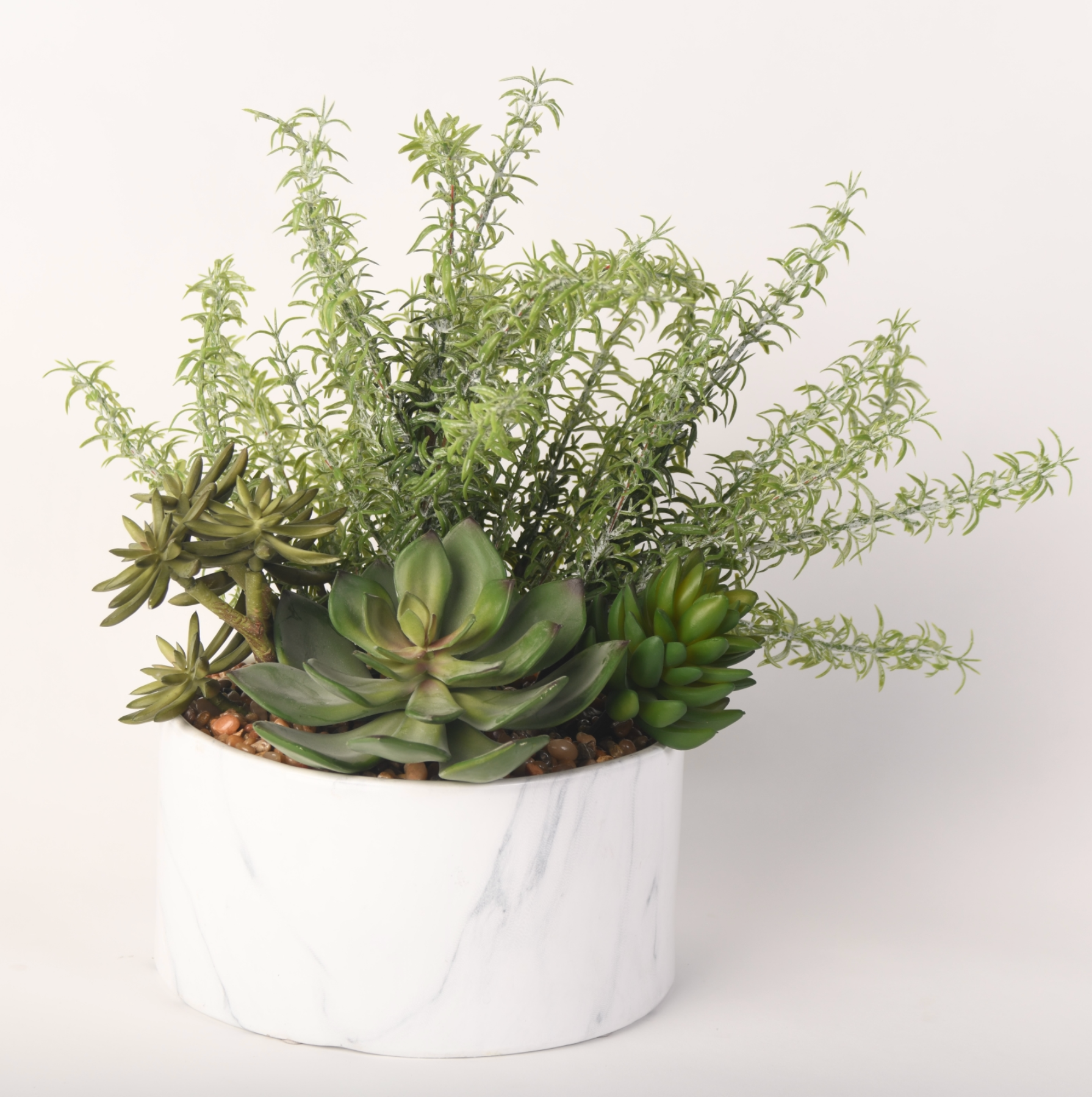 An artificial succulent and shrub arrangement in a round white marble-look planter.
