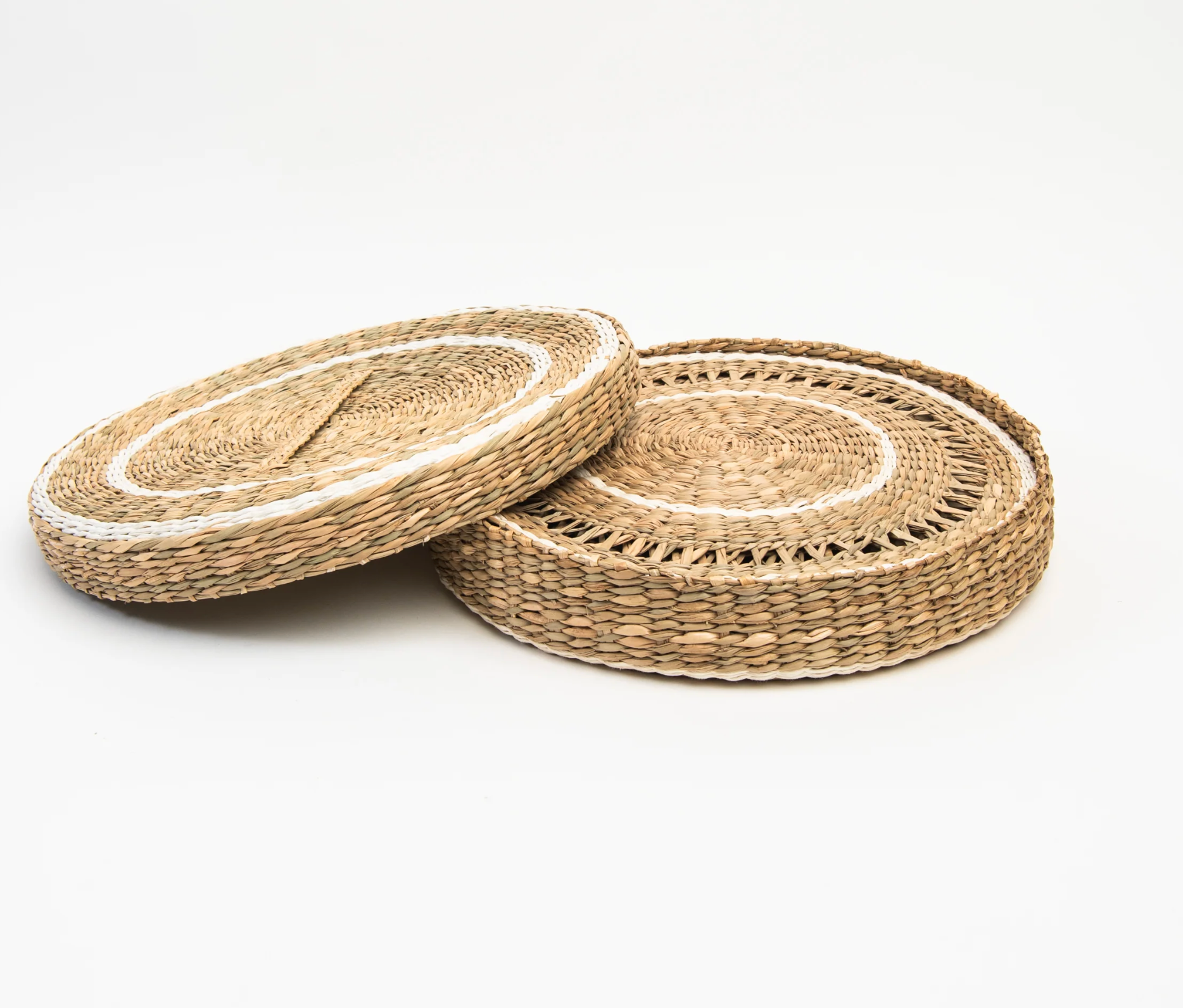 Two round woven seagrass or straw placemats with a natural tan color and white braided accents.