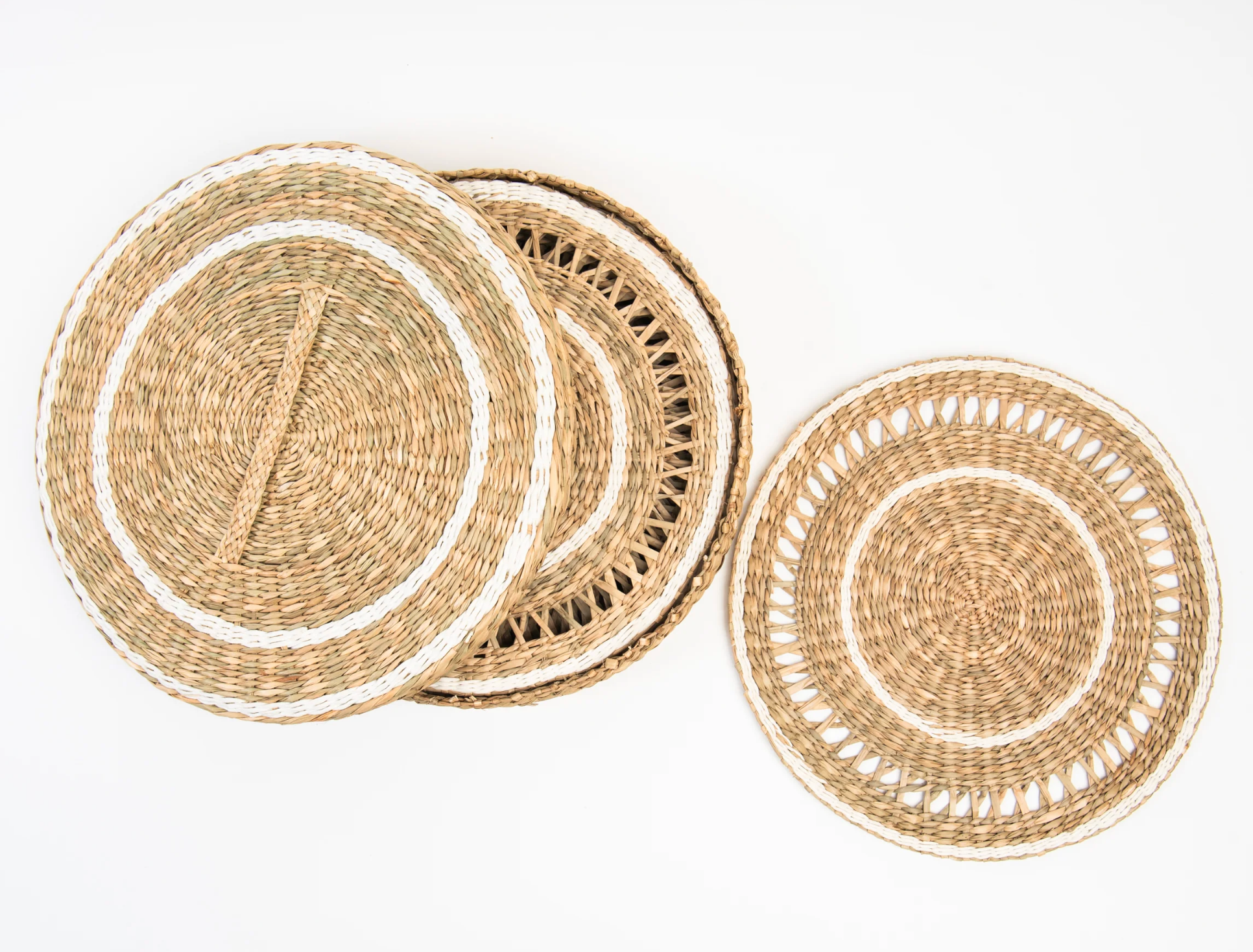 Three round woven seagrass placemats in natural beige and white tones.