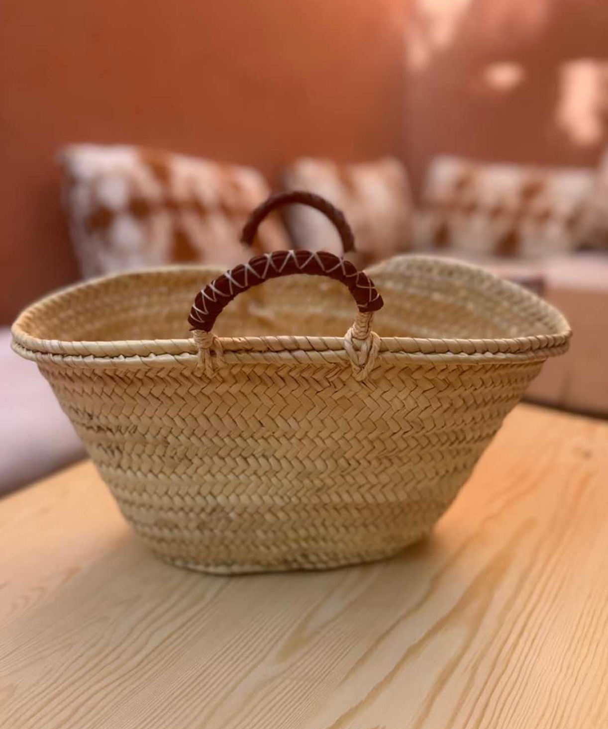 A natural woven straw basket with a dark brown leather handle.