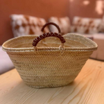 A natural woven straw basket with a dark brown leather handle.