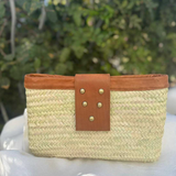 A woven straw clutch bag with a tan leather strap and gold-tone studs.