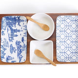 A set of porcelain and bamboo serving pieces with a blue floral pattern, including two bowls, two rectangular plates, and one acacia wood tray.