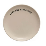 A round off-white ceramic plate with the text 'AGED AND EXTRA FINE' printed in black.