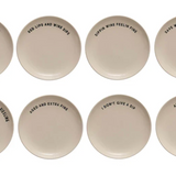 Eight round ceramic coasters in a warm off-white color, arranged in two rows of four on a plain white background. Each coaster features a different humorous phrase printed in black sans-serif font.