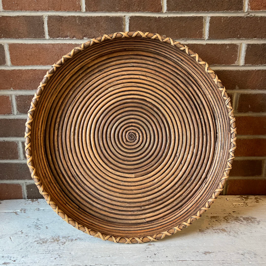 A round woven rattan tray with a spiral pattern and a decorative scalloped edge.